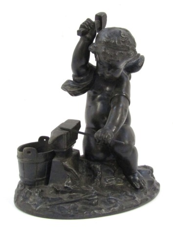 A bronze figure group of a cherub, modelled beside a blacksmiths, on an oval base, with applied green velvet protection layer, 15cm high.