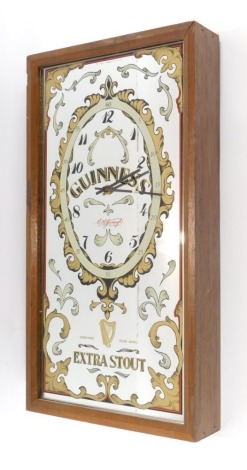 A Guinness extra stout advertising clock, with mirrored glass front in a mahogany fitted case, 29cm wide, 54cm high, 8cm deep.