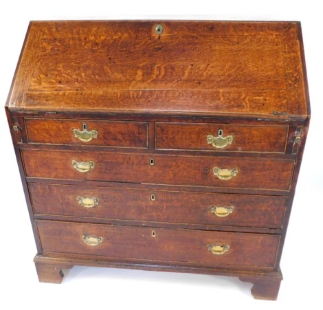 A George III oak bureau, the fall opening to reveal a fitted interior above two short and three long drawers, with brass handles on bracket feet, 120cm high, 101cm wide, 50cm deep.