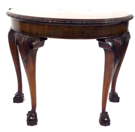 A late 19thC mahogany demi lune table, with a carved border, on cabriole legs and ball and claw feet, 75cm high, 92cm wide, 48cm deep.