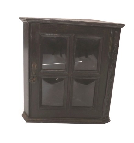 A late 19thC oak corner cabinet, the door four convex glazed panels, with Art Nouveau style brass applied handle, and one carved side, 48cm high, 46cm wide, 26cm deep at the widest point.