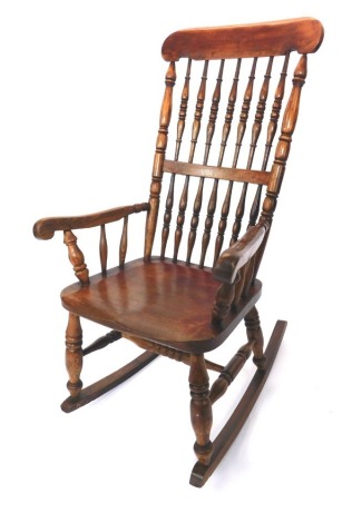 A 19thC ash rocking chair, with spindle back and scroll carved arms, on turned legs, 110cm high, 58cm wide, 75cm deep.