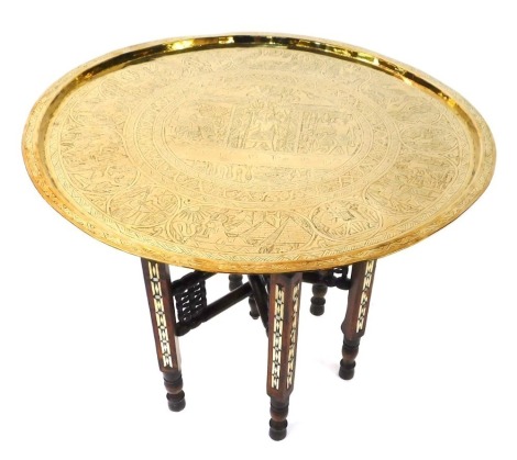 An Egyptian brass table, the brass top tray with embossed detailing of figures and animals on a walnut base with mother of pearl inlay, 56cm high, 63cm diameter.