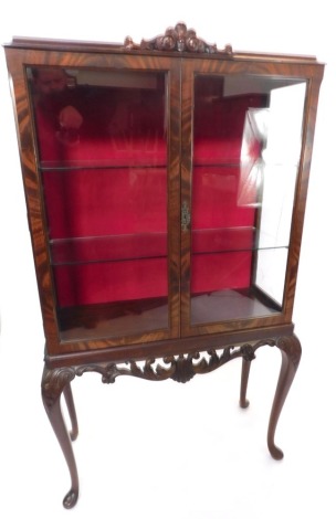 A reproduction mahogany display cabinet, with carved crest, above two glazed doors, a red lined backing and two shelves, on cabriole legs, 152cm high, 85cm wide, 35cm deep. (AF)