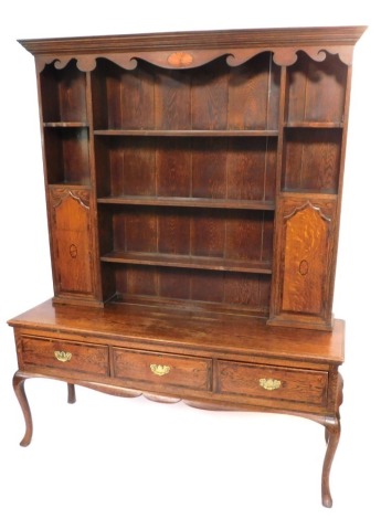 An Edwardian oak dresser, the top with a raised cornice and shaped apron with marquetry fan, on three shelves, two cupboards, the base with three drawers, on cabriole legs, 210cm high, 168cm wide, 50cm deep.