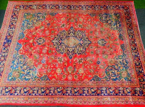 A 20thC Iranian carpet, rectangular with outer floral field predominantly in red, blue and green, with a floral centre, 380cm x 290cm.