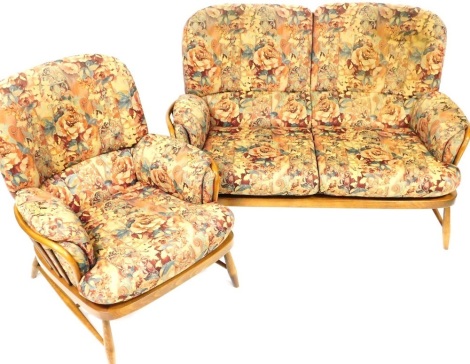An Ercol Jubilee dark elm and beech cottage two seater sofa and matching armchair, each with a stick back and floral upholstery, on turned legs with h stretcher, the sofa 130cm wide.