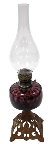 An early 20thC cast iron and brass oil lamp, with an amethyst glass reservoir, glass chimney, raised on a foliate scroll base, 54cm high.