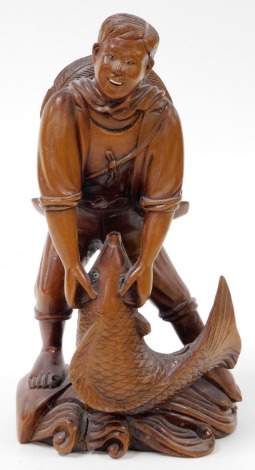 An Oriental carved wooden figure of a fisherman, modelled crouched over a large fish, on a naturalistic base, 25cm high.