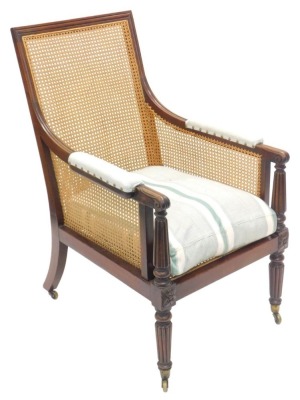 An early 19thC mahogany bergere library armchair, with a moulded frame, padded arm rests, reeded arm supports and legs, with casters.