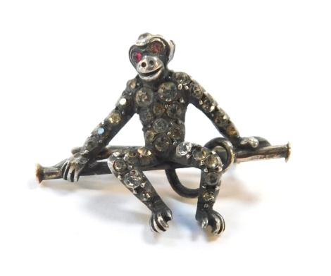 An Edwardian monkey brooch, formed as a monkey perched on bar, set with white and red paste stones, white metal stamped 925, 2.5cm wide, 4.8g all in.