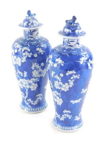 A pair of Chinese Qing Dynasty porcelain prunus vases, each with inverted shouldered form with domed lids set with animal knops, four character marks beneath, 26cm high. (AF) (2)