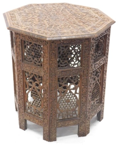 A carved Indian and hardwood occasional table, the octagonal top elaborately decorated with leaves, scrolls, etc., the folding base with pierced decoration, 50cm high, 44cm wide.