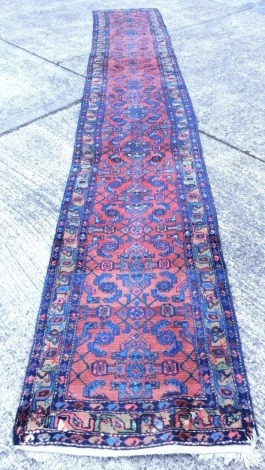 A 20thC Persian runner, of rectangular form with a central field of diamond geometric floral pattern, with an outer border of further flowers predominantly in red and blue, approx 480cm x 76cm.