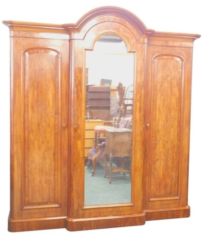 A Victorian figured mahogany breakfront wardrobe, with an arched moulded crest, above a mirrored door flanked by two panelled doors enclosing fittings, on a plinth, 228cm high, 204cm wide.