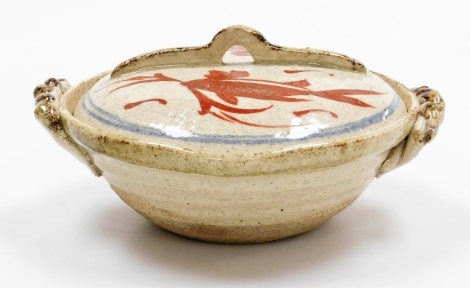 A 20thC Japanese folk art two handled bowl and cover, painted with fish in iron red, with pouring lip, 15.5cm diameter.