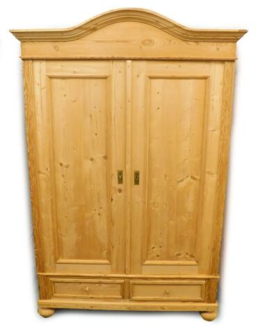 A continental pine armoire or wardrobe, with a moulded cornice above two panelled doors enclosing a hanging rail, base with two drawers, on bun feet, 144cm wide.