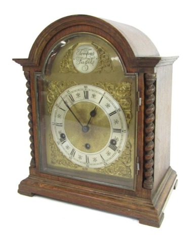 An early 20thC oak cased mantel clock, with brass and silvered coloured dial, with a Roman numeric chapter ring and applied gilt detailing of Tempus Fugit, with domed top and barleytwist column, black feet, 36cm high, 30cm wide, 18cm deep,