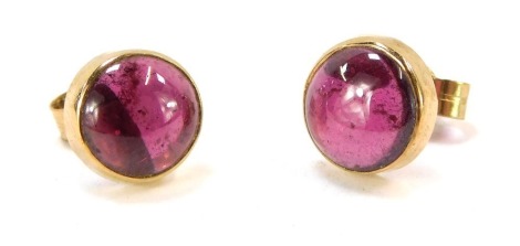 A pair of stud earrings, each with a cabochon purple coloured stone, in rub over setting, with a stick pin back and butterfly backs, yellow metal stamped 9ct, 1.6g all in.