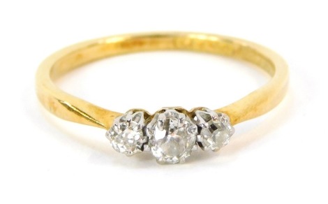 A three stone diamond dress ring, with three round brilliant cut diamonds, each in platinum claw setting on a yellow metal band marked 18ct plat, ring size O½, 2.2g all in.