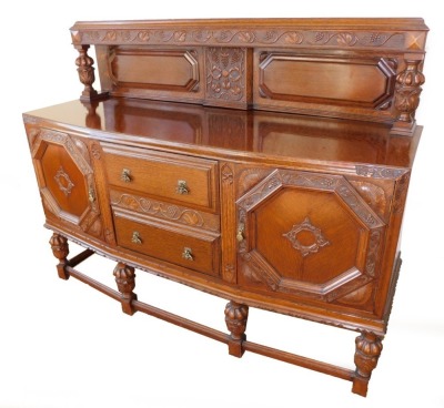 An early 20thC oak sideboard, the back carved carved with vines, over two drawers flanked by carved panelled doors, the left enclosing shelves, right enclosing a bottle holder, all raised on acanthus leaf carved and semi fluted cup and cover supports, the