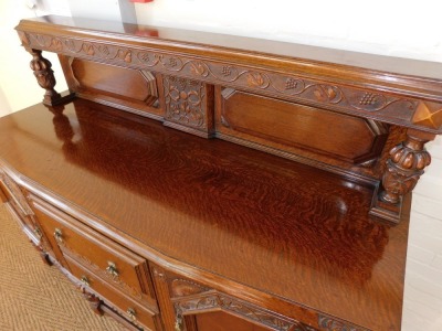 An early 20thC oak sideboard, the back carved carved with vines, over two drawers flanked by carved panelled doors, the left enclosing shelves, right enclosing a bottle holder, all raised on acanthus leaf carved and semi fluted cup and cover supports, the - 2