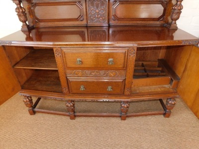 An early 20thC oak sideboard, the back carved carved with vines, over two drawers flanked by carved panelled doors, the left enclosing shelves, right enclosing a bottle holder, all raised on acanthus leaf carved and semi fluted cup and cover supports, the - 3