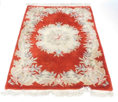 A Chinese cut wool rug, on a red ground with cream flowers, and tassel ends, 187cm x 125cm.