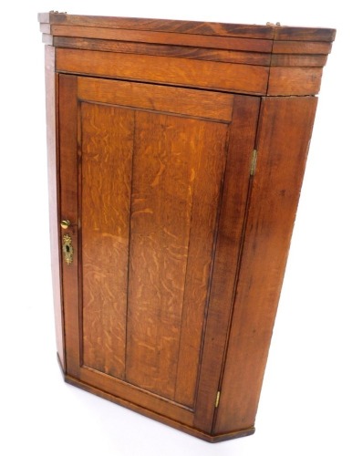 A 19thC oak hanging corner cupboard, the pediment above a single panelled door, with brass handle and escutcheon, enclosing three shelves, 102cm high, 68cm wide, 39cm deep.