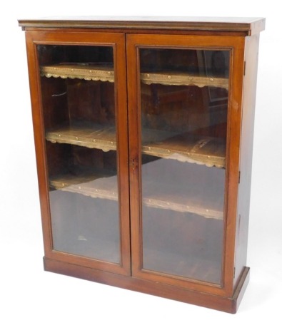 A Victorian mahogany bookcase, the pediment over a pair of glazed doors, enclosing three adjustable shelves, gold velvet covered with a leather trim to the front, raised on a plinth base, 122cm high, 98cm wide, 31cm deep.