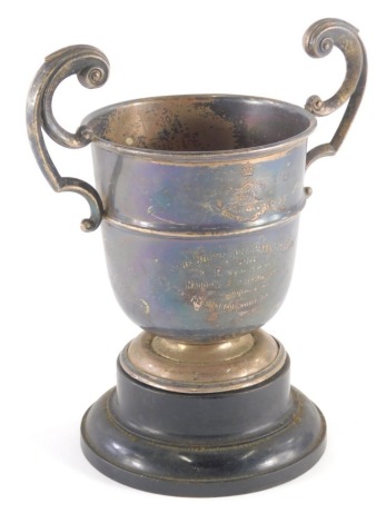 An Edwardian silver trophy, with flying scroll handles and bell shaped body on circular foot, partially engraved the Dickinson Challenge Cup, 1908, Lincolnshire, on ebonised stand, Chester 1908, 19cm high, 6½oz.