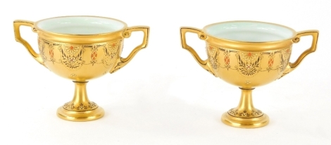 A pair of miniature Royal Worcester porcelain vases, each gilt decorated with a floral banding in black and red, on circular feet, with ear shaped handles, printed marks beneath, 8cm high. (2, AF)