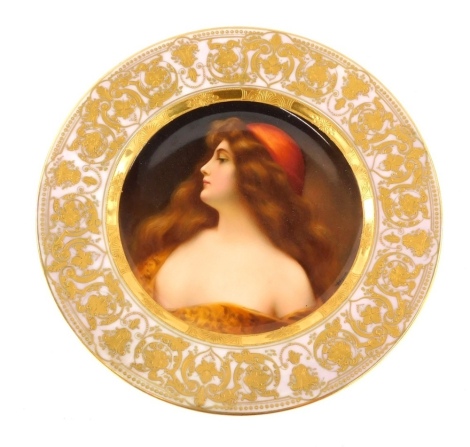 A 19thC Vienna porcelain cabinet plate, decorated with a portrait of a young lady with flowing brown hair and a red hat, titled Una Gitana, signed Wagner, within a pink and elaborate gilt border, 24.5cm diameter.