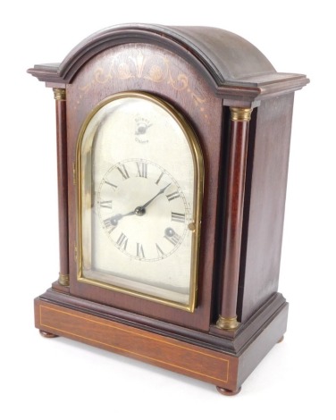 An Edwardian mahogany table clock, in arched case, the 12cm wide silvered etched Roman Numeric dial flanked by cylindrical columns on compressed bun feet, with silent/chime, 8 day chiming key wind movement with pendulum, 34cm high.