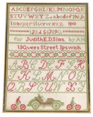 An Edwardian and early provincial automotive pictorial alpha numeric needlework sampler, dated 1910, named 'For Judith E.D. Sims by AH', 13 Queen Street, Ipswich, over images of bicycles and an Edwardian motor car, glazed and framed, 41cm x 30cm.