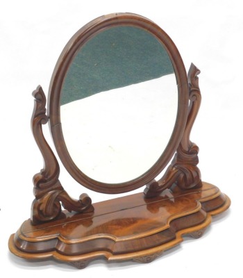 A Victorian figured mahogany dressing table mirror, the oval plate on carved supports, the serpentine fronted face with a hinged trinket compartment on tapering feet, 85cm wide.