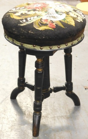 A Victorian ebonised and parcel gilt adjustable piano stool, the circular top decorated with woolwork and beaded flowers on turned legs and splayed feet, 48cm high, 33cm diameter.