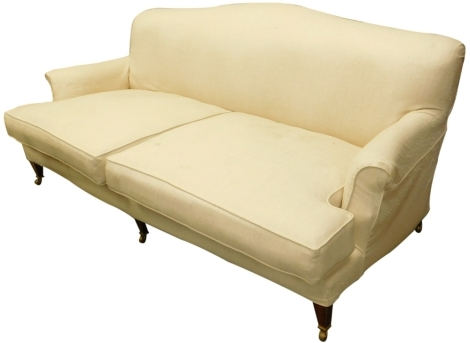 A mahogany three seater sofa, with cream upholstery, on square tapering legs with castors, in the manner of Howard and Sons, 202cm wide. The upholstery in this lot does not comply with the 1988 (Fire & Fire Furnishing) Regulations, unless sold to a known