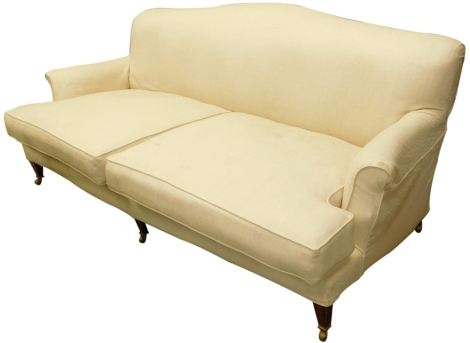 A mahogany three seater sofa, with cream upholstery, on square tapering legs with castors, in the manner of Howard and Sons, 202cm wide. The upholstery in this lot does not comply with the 1988 (Fire & Fire Furnishing) Regulations, unless sold to a known