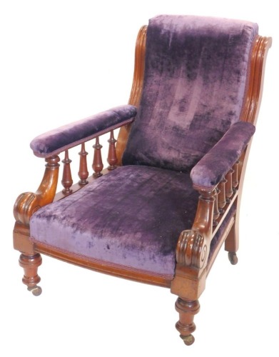 A Victorian mahogany armchair, upholstered in purple velvet, with moulded frame and turned arm supports, scrolling arms on turned legs with castors,