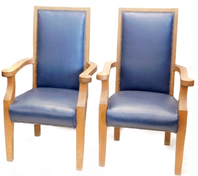 A pair of oak library type armchairs, each with a blue padded leatherette back and seat, shaped arms on square tapering legs.