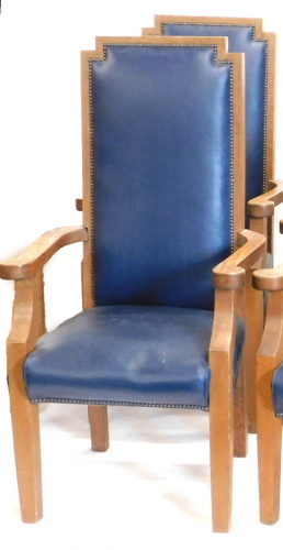 A pair of oak library type armchairs, each with a blue leatherette padded high back and seat, shaped arms on square tapering legs.