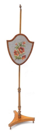 An early 19thC satinwood tulipwood cross banded and beech pole screen, the shield shaped banner with later floral wool work, the concave base supported by turned tapering feet, adapted, 147cm high overall.