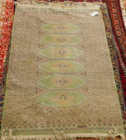 An Afghan rug, with a design of six latch hook medallions, on a green ground with multiple geometric borders, 184cm x 125cm.