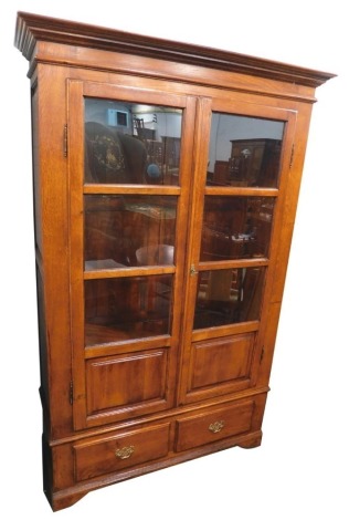 An oak bookcase, the top with a moulded cornice above two glazed and panelled doors enclosing adjustable shelves, above two plinth drawers, on bracket feet, 200cm high, 130cm wide, 46cm deep.