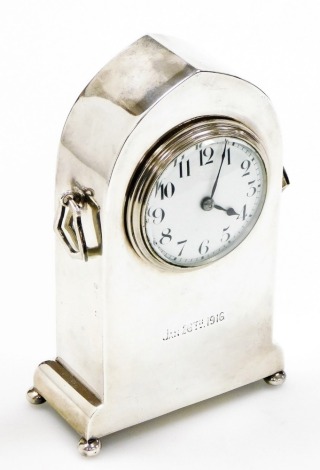 An early 20thC silver cased mantel clock, in a plain lancet shaped case, with two ring handles, the white enamelled dial bearing Arabic numerals, raised on four ball feet, the case engraved Jan 26th 1916, hallmarks rubbed, 16cm high.
