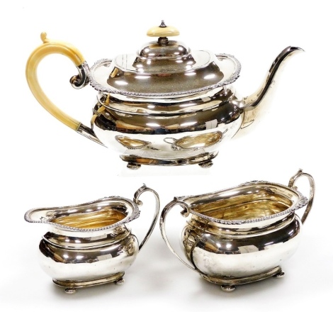 An Edward VII silver three piece tea set, comprising teapot, milk jug and two handled sugar bowl, the teapot with an ivory knop and handle, each piece decorated with a gadrooned, shell and foliate cast border, raised on four bun feet, Harrison Brothers an