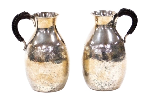 A pair of Japanese silver sake ewers, with leather bound handles, of bulbous form with textured decoration, four character Jungin (silver) mark, 11.5cm high.