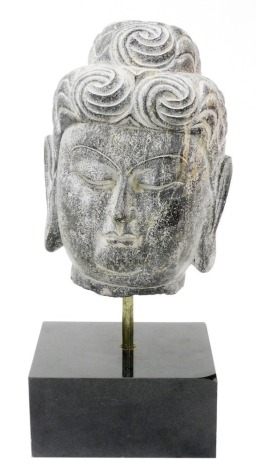 A 20thC stone carved Buddha head, mounted on a black marble base, 58cm high.