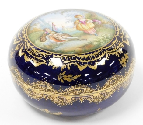 A 19thC Bohemian porcelain circular box and cover, depicting a gentleman playing a musical instrument to a lady, against a dark blue ground with gilt highlights, the interior decorated with flowers, painted beehive mark, 10cm high, 15cm diameter.